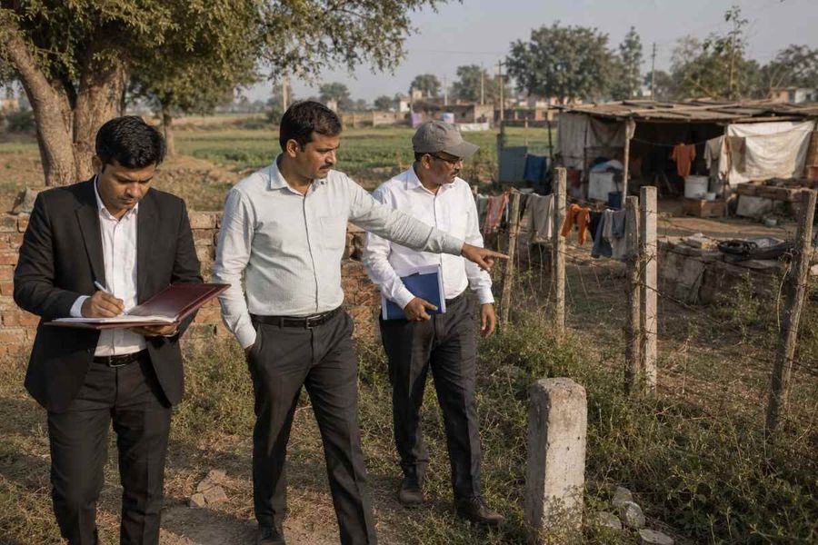 Property owners and a legal advisor inspecting an agricultural land boundary and reviewing property records during a site verification in India.