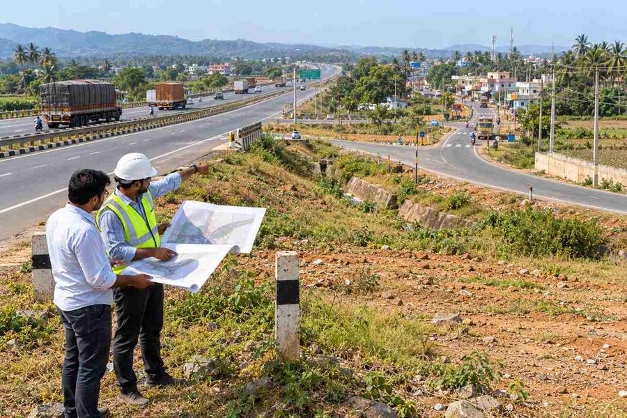 Two men reviewing a site plan on open land beside a national highway near a growing town