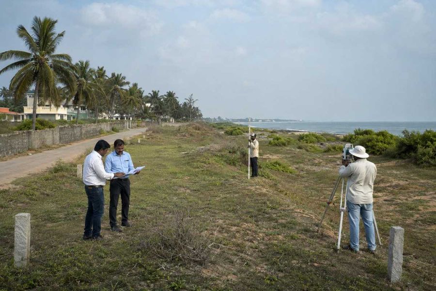Surveyors measuring distance from the high tide line using a total station along the coast.