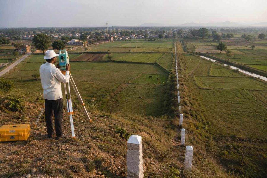 Surveyor using a total station overlooking a long row of boundary markers dividing farmland.